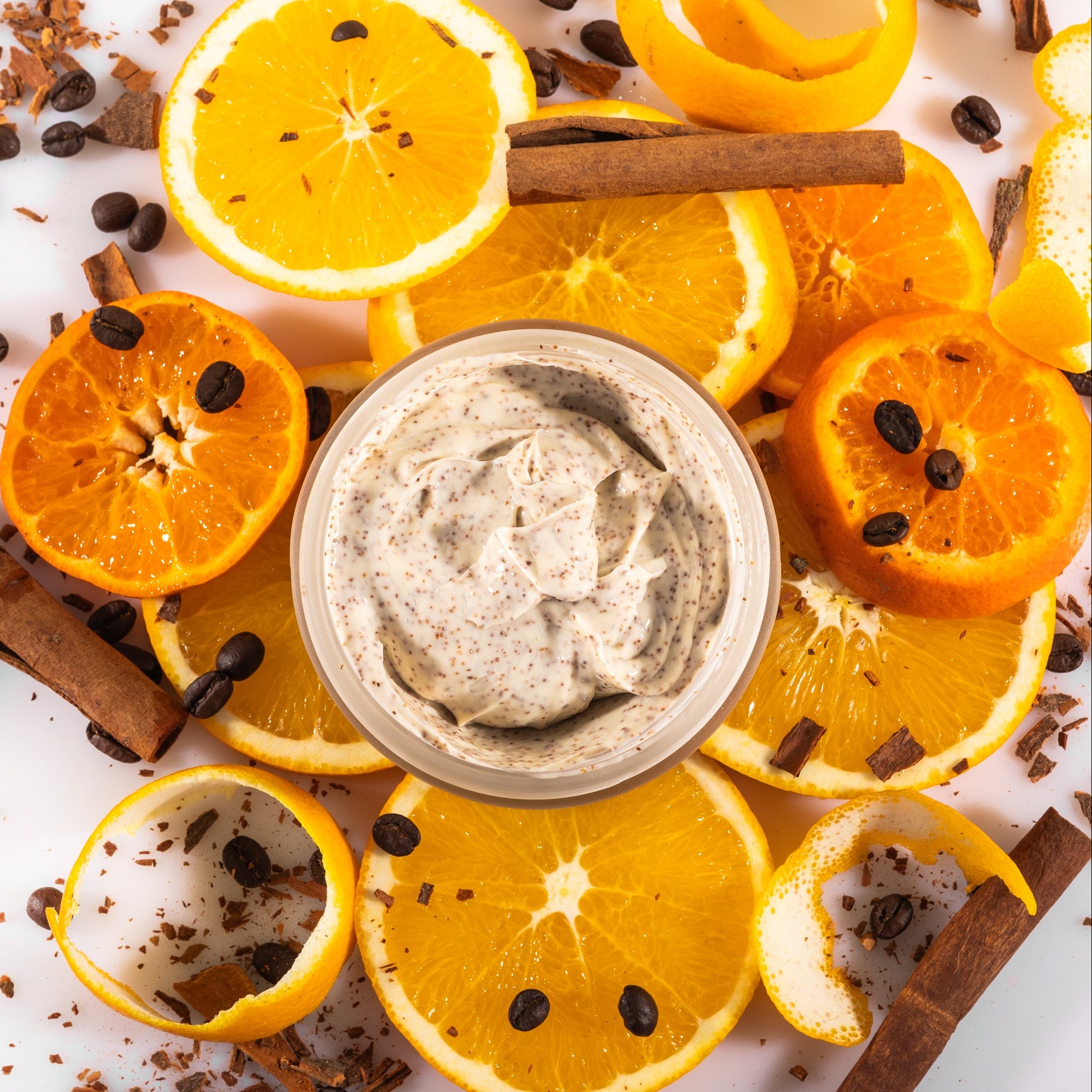 Body Polish on top of orange slices, coffee beans, and cinnamon on a white background
