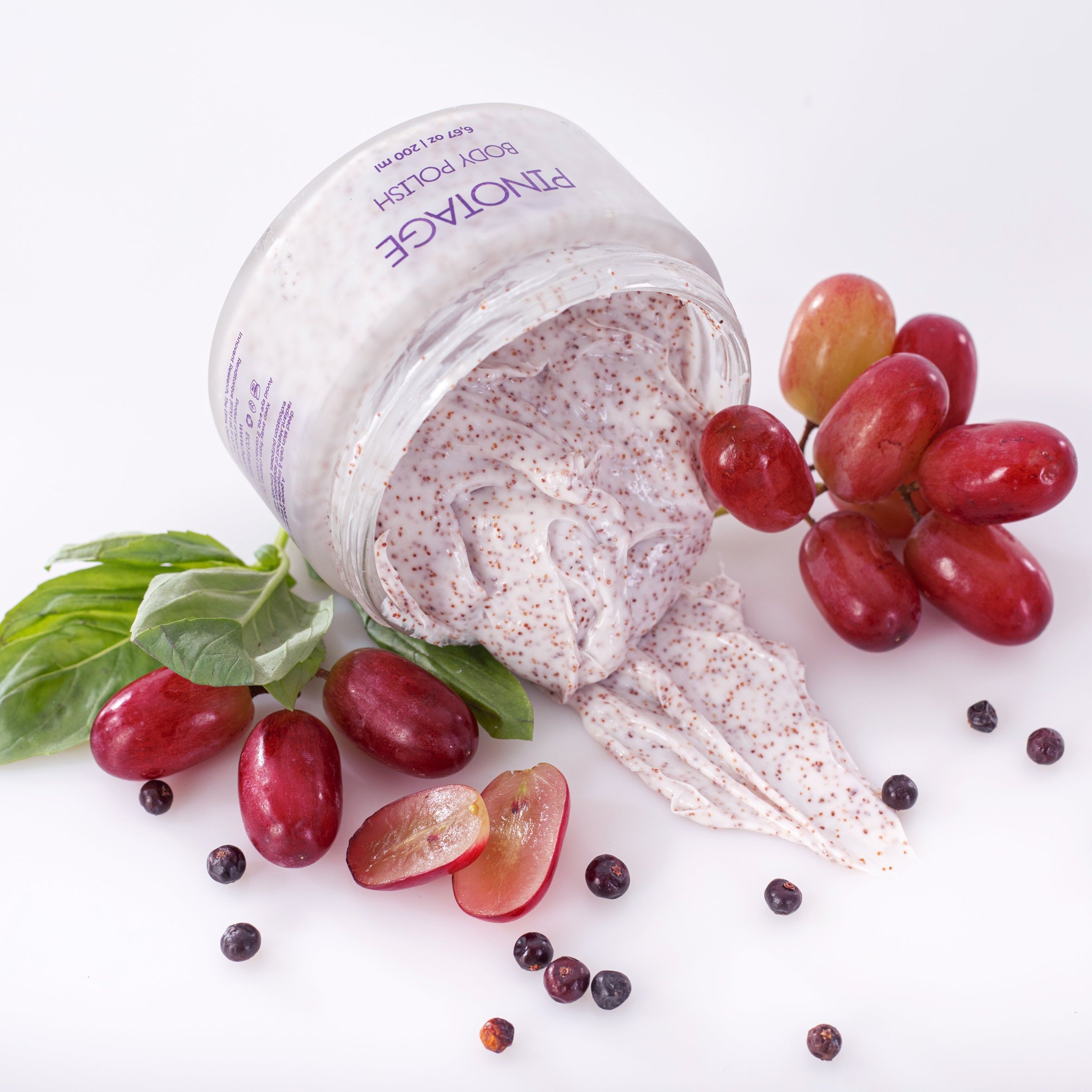 Container of Pinotage Body Polish with grapes and other fruits on a white background